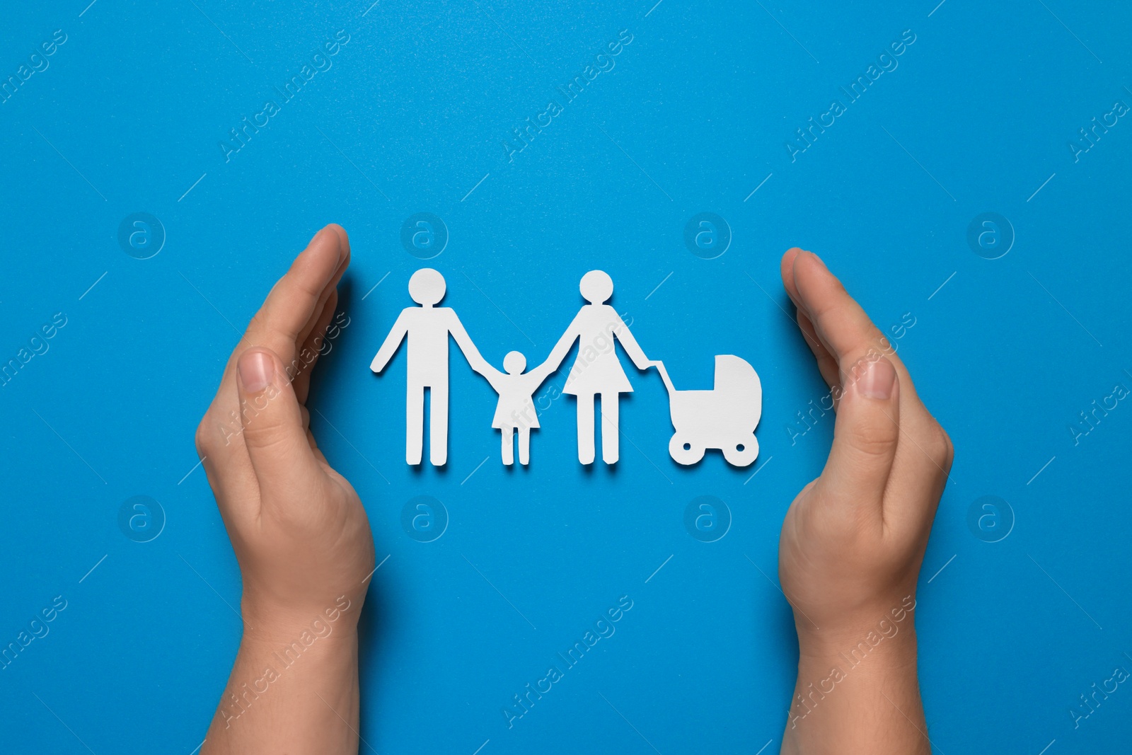 Photo of Man protecting paper family figures on light blue background, top view. Insurance concept
