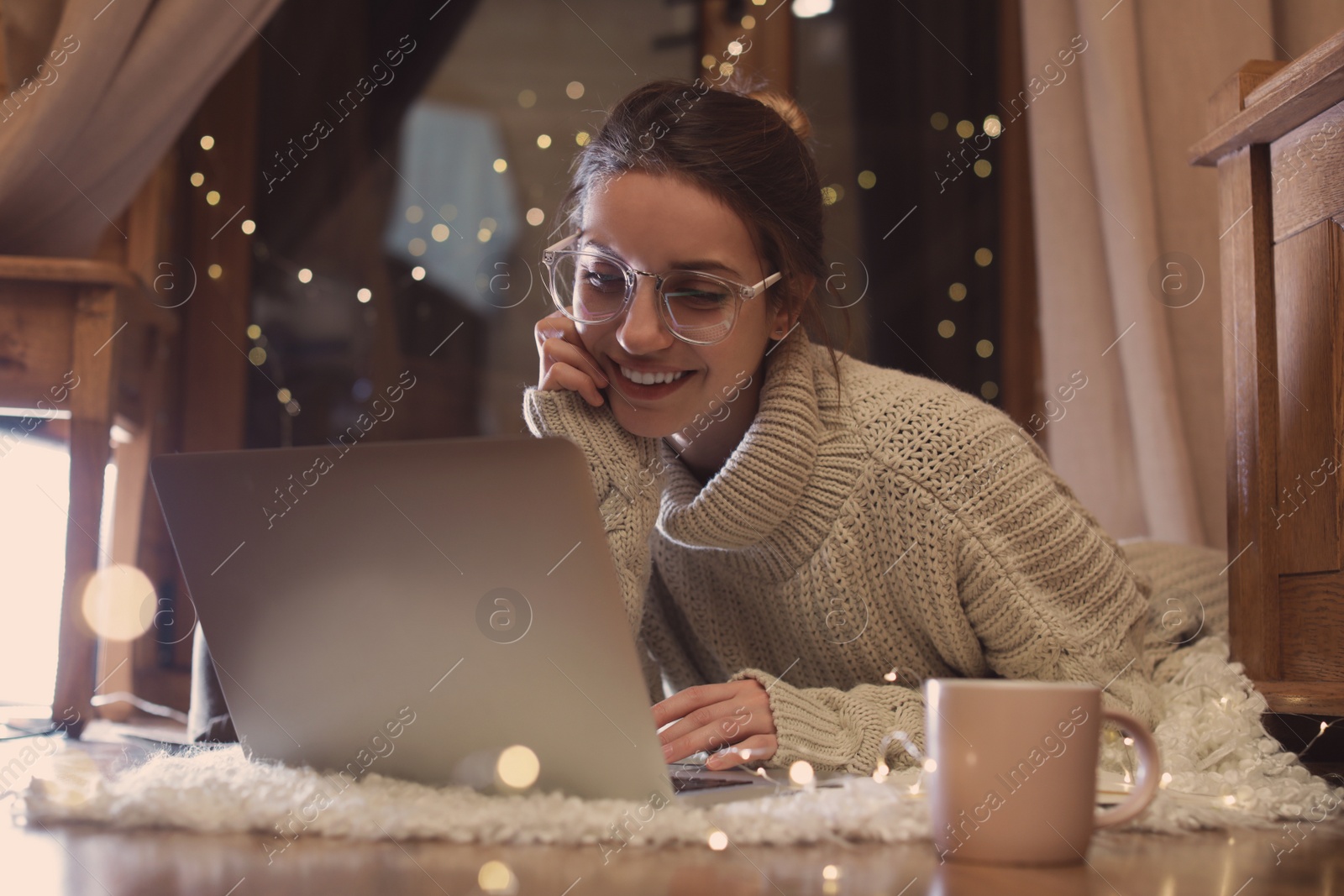 Photo of Woman with cup of hot beverage using laptop at home in winter evening