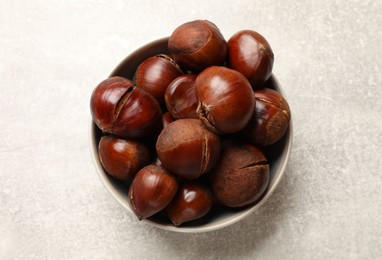 Fresh edible sweet chestnuts in bowl on grey table, top view