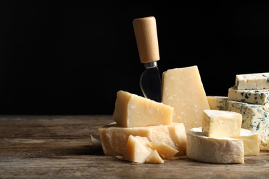 Photo of Different sorts of cheese and knife on wooden table against black background. Space for text