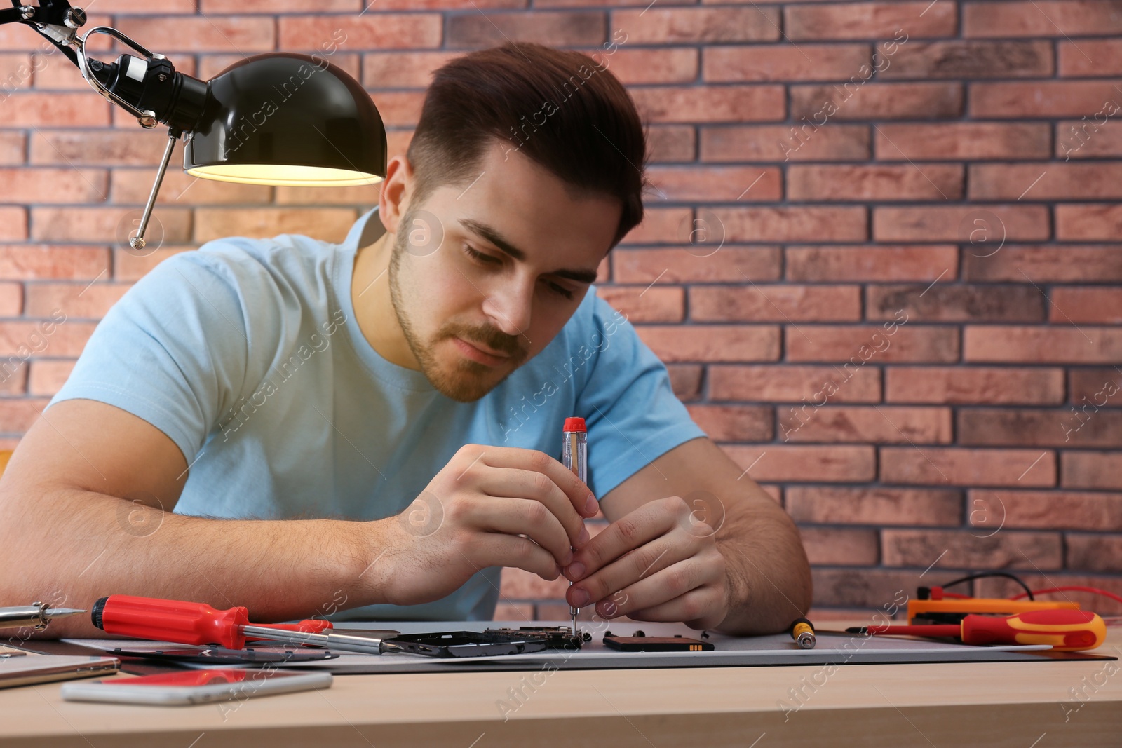 Photo of Technician repairing broken smartphone at table in workshop