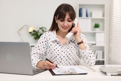 Smiling secretary talking on telephone at table in office