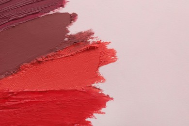 Photo of Smears of different beautiful lipsticks on light background, top view. Space for text