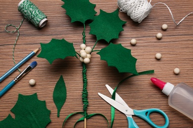 Photo of Set of instruments and materials for making mistletoe branch on wooden table, flat lay