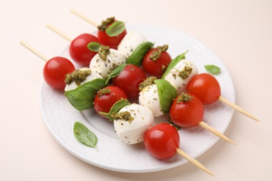 Photo of Caprese skewers with tomatoes, mozzarella balls, basil and pesto sauce on beige background, closeup