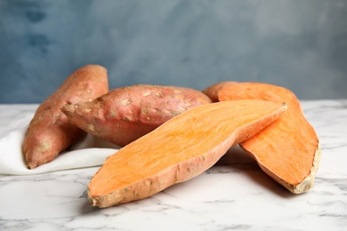 Photo of Sweet potatoes on marble table against color background