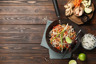 Shrimp stir fry with noodles and vegetables in wok on wooden table, flat lay. Space for text