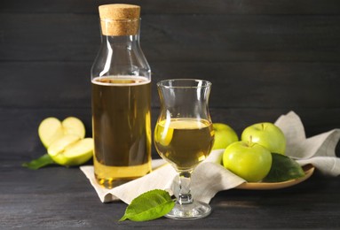 Delicious cider and apples with green leaves on black wooden table