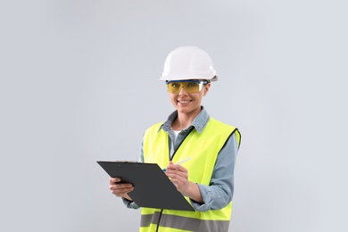 Female industrial engineer in uniform with clipboard on light background. Safety equipment