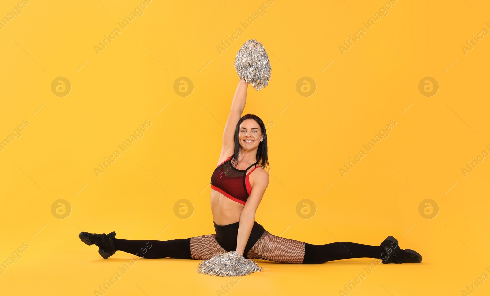 Photo of Beautiful cheerleader in costume holding pom poms on yellow background