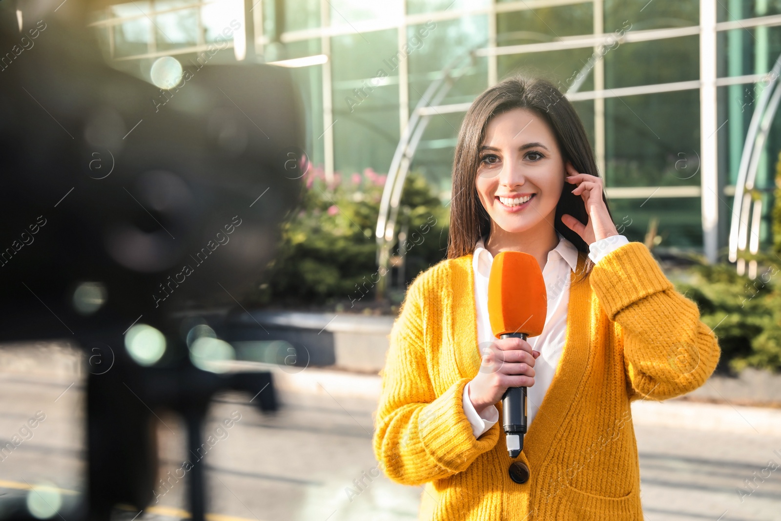 Image of Young female journalist with microphone working on city street