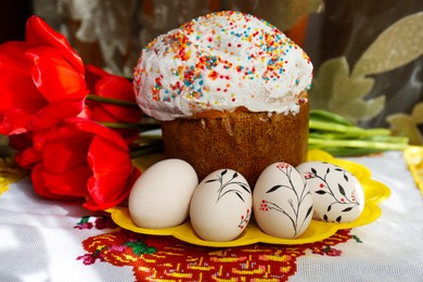 Photo of Eggs with floral ornaments and kulich for Easter near bouquet of red tulips on table