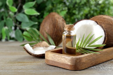 Photo of Bottle of organic coconut cooking oil, fresh fruits and leaf on wooden table, closeup. Space for text