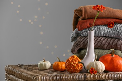 Beautiful autumn flowers, pumpkins and stacked clothes on wicker table, space for text