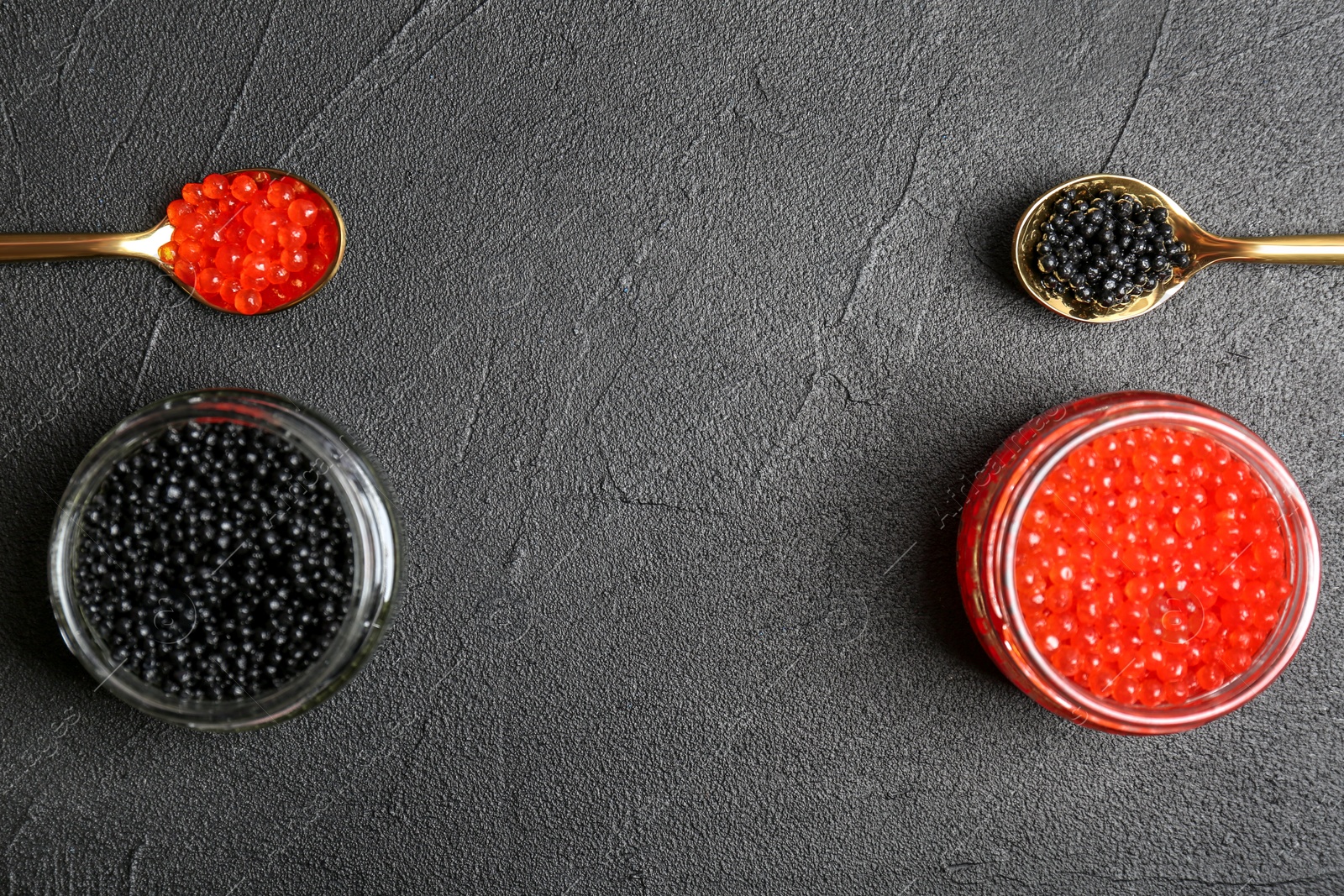 Photo of Glass jars and metal spoons with black and red caviar on grey background