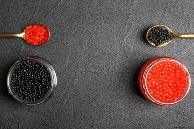 Glass jars and metal spoons with black and red caviar on grey background