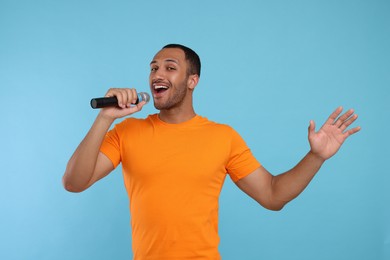 Handsome man with microphone singing on light blue background