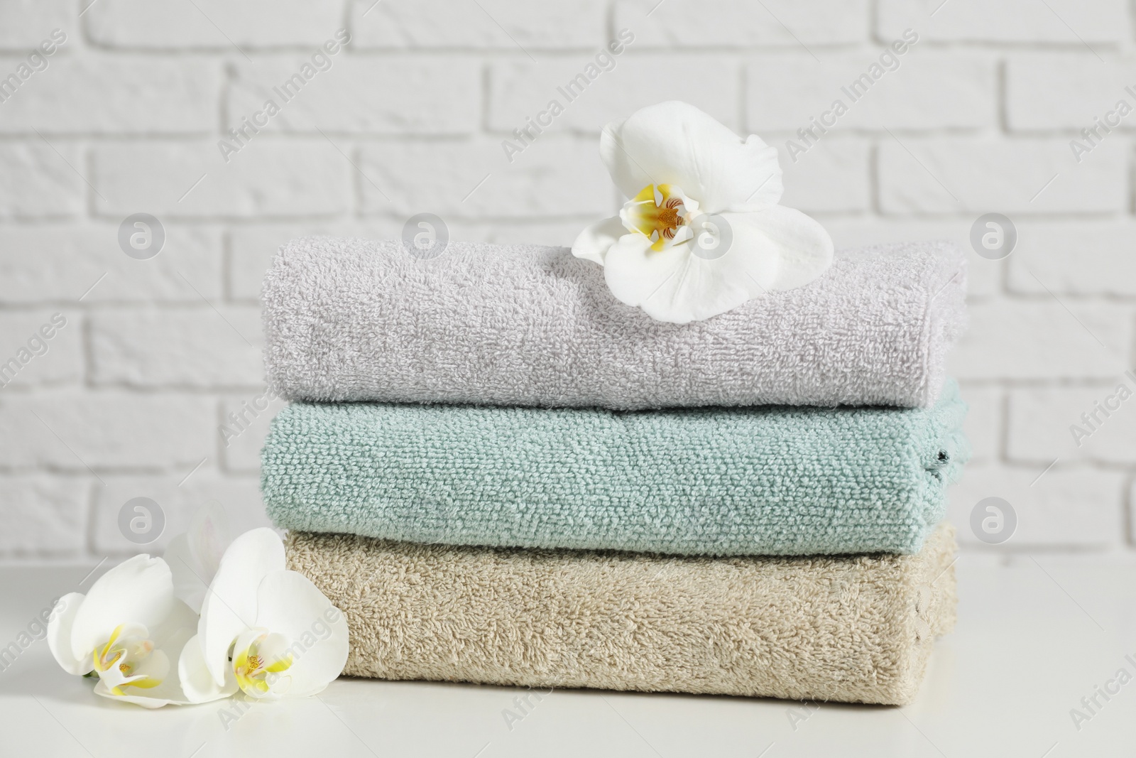 Photo of Clean soft towels with flowers on table near white brick wall