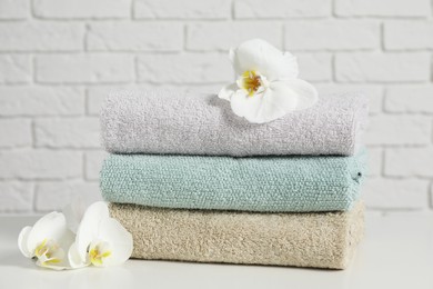 Photo of Clean soft towels with flowers on table near white brick wall