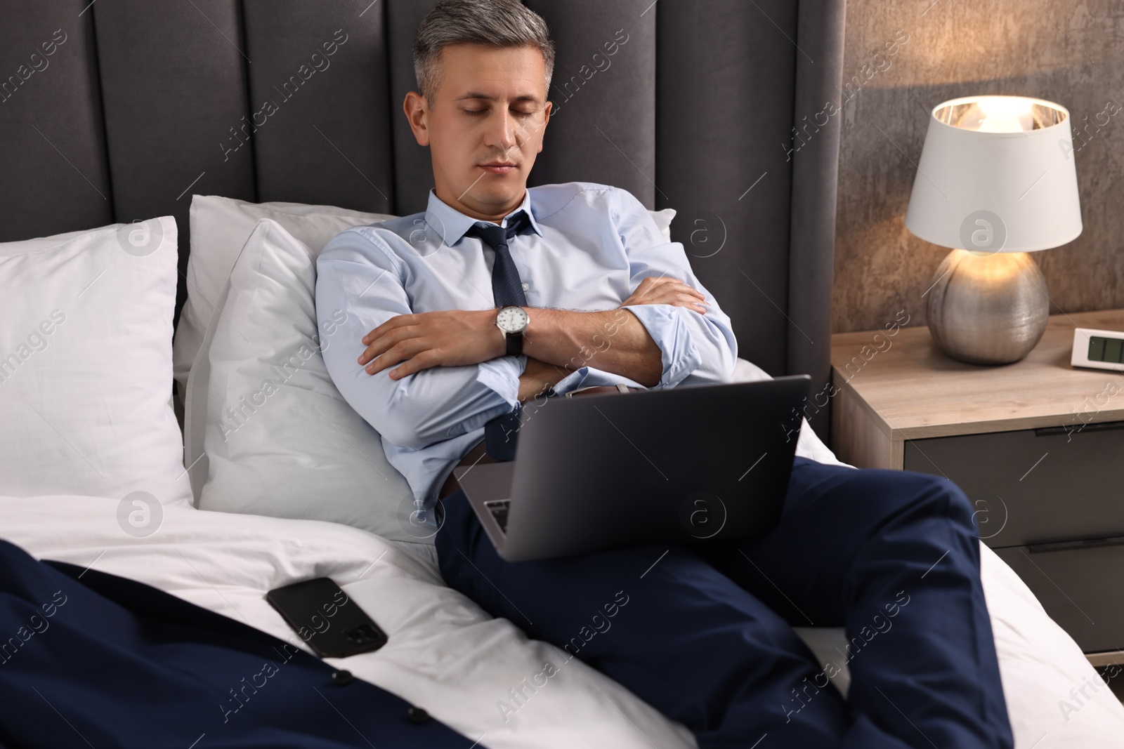 Photo of Businessman with laptop sleeping on bed indoors