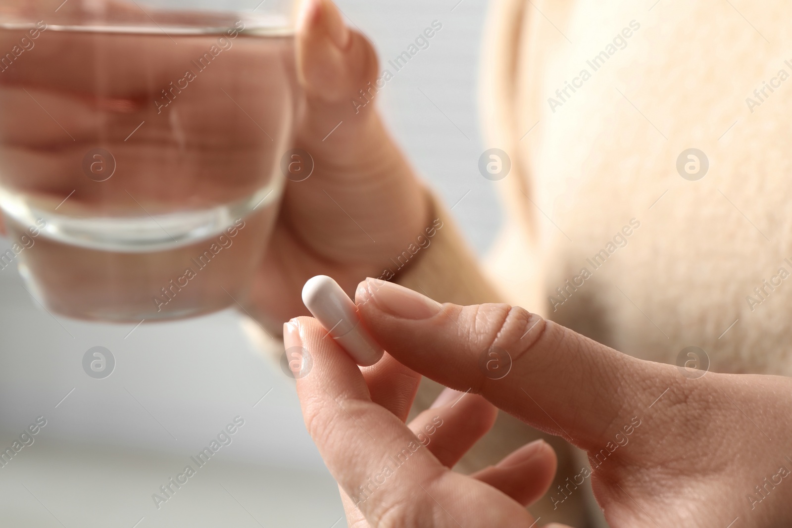 Photo of Woman with pill and glass of water on blurred background, closeup