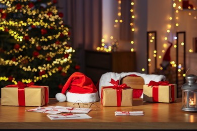 Photo of Santa's Claus workplace. Gift boxes, letters, lantern on table and costume in room with Christmas decor