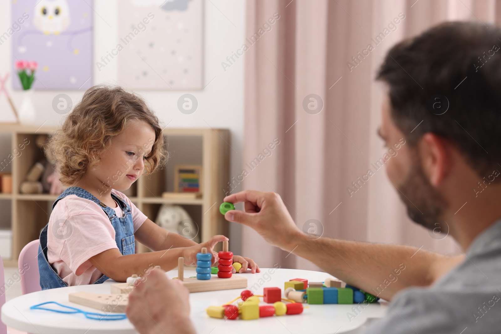 Photo of Motor skills development. Father and daughter playing with stacking and counting game at table indoors