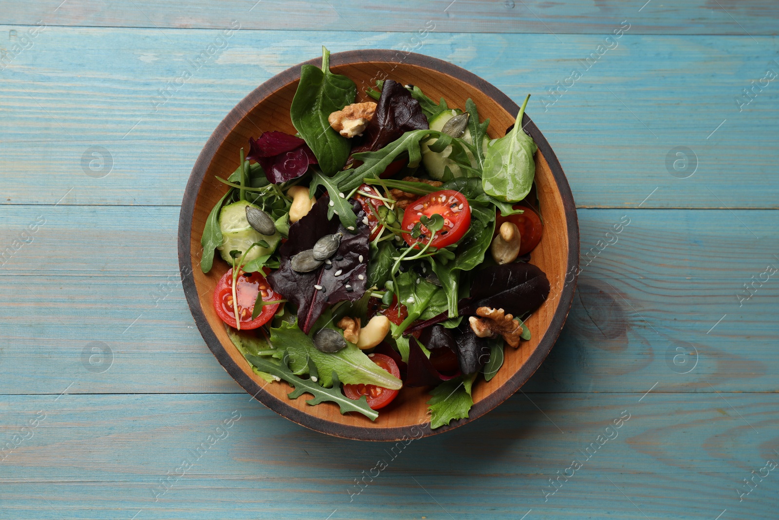 Photo of Tasty fresh vegetarian salad on light blue wooden table, top view