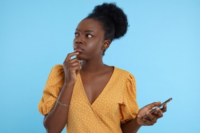 Photo of Concentrated young woman with smartphone on light blue background