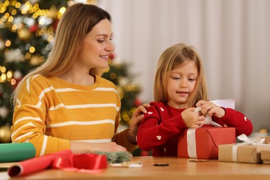 Christmas presents wrapping. Mother and her little daughter decorating gift box with ribbon at home