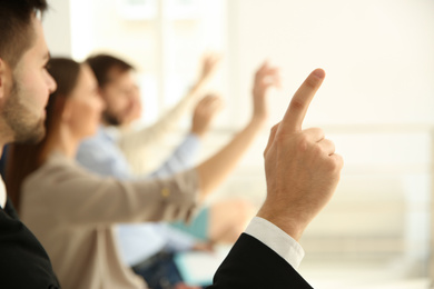 Young man raising hand to ask question at business training indoors, closeup