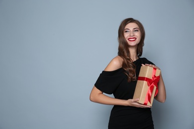 Happy woman with gift box on grey background, space for text. Christmas party