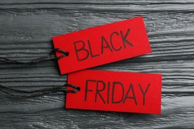 Photo of Red tags with words BLACK FRIDAY on dark wooden background, flat lay