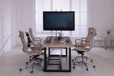 Photo of Interactive board near wooden table and chairs in meeting room