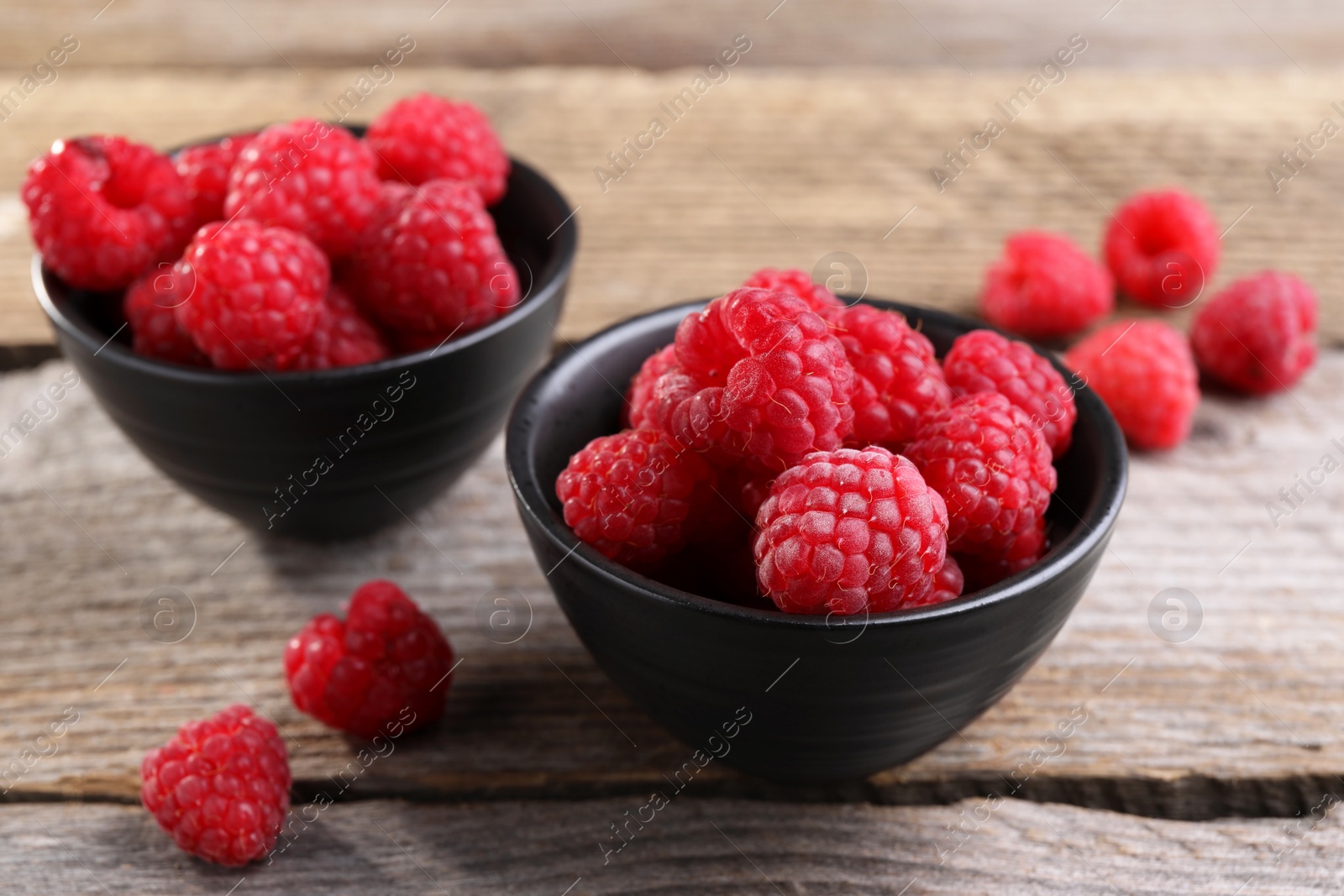 Photo of Tasty ripe raspberries in bowls on wooden table