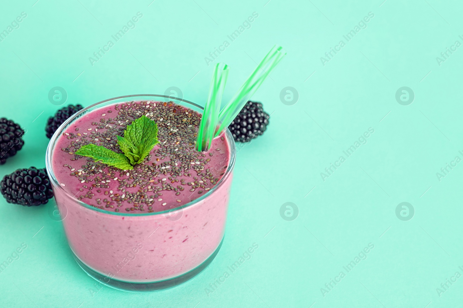 Photo of Glass of tasty blackberry smoothie with chia seeds and straws on turquoise background. Space for text