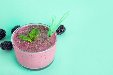 Glass of tasty blackberry smoothie with chia seeds and straws on turquoise background. Space for text