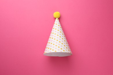 Photo of One party hat with hearts on pink background, top view