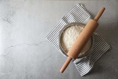 Photo of Flour in bowl, rolling pin and napkin on grey table, top view. Space for text