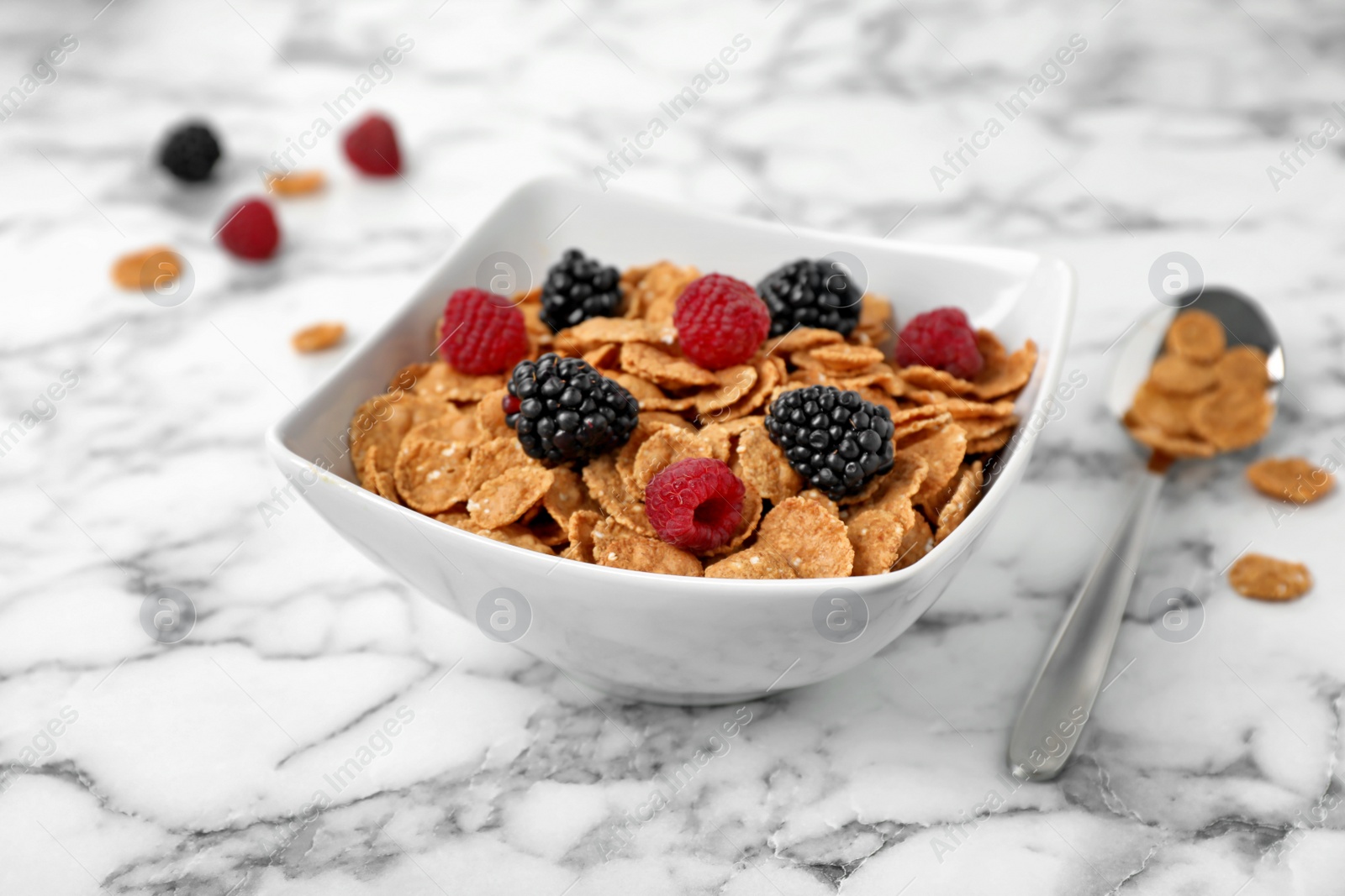 Photo of Bowl with cornflakes and berries on marble table. Whole grain cereal for breakfast