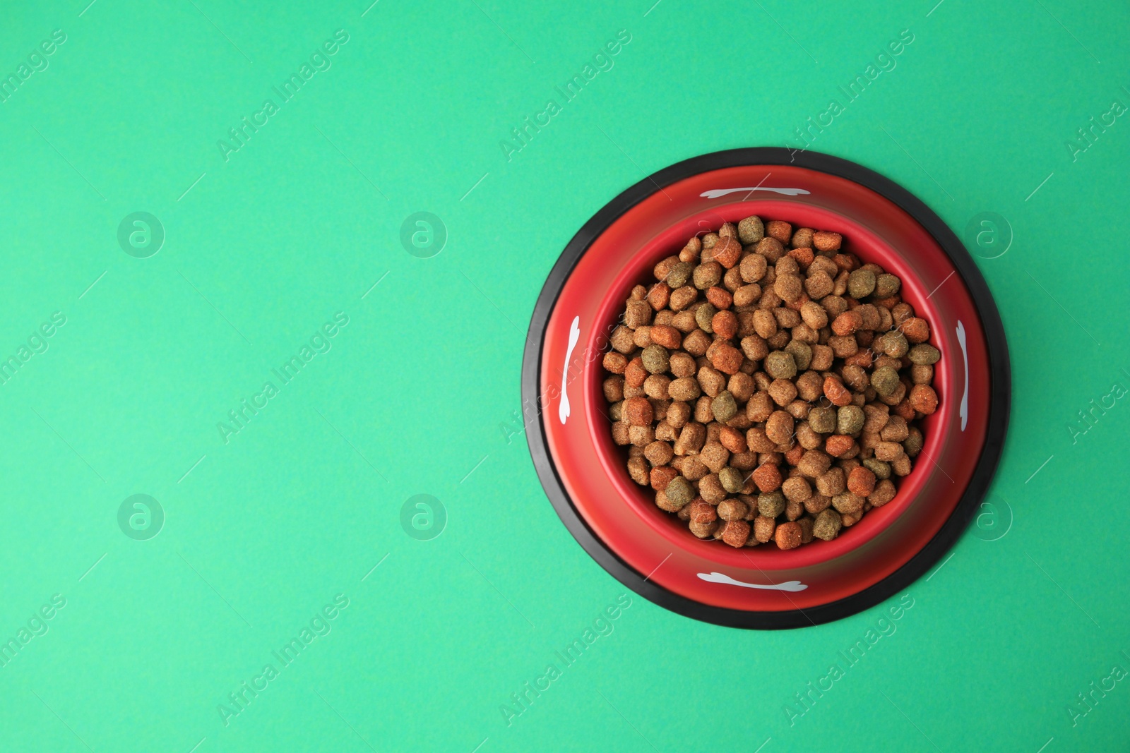 Photo of Dry dog food in feeding bowl on green background, top view. Space for text