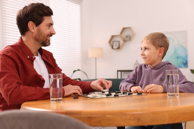 Family playing checkers at wooden table in room