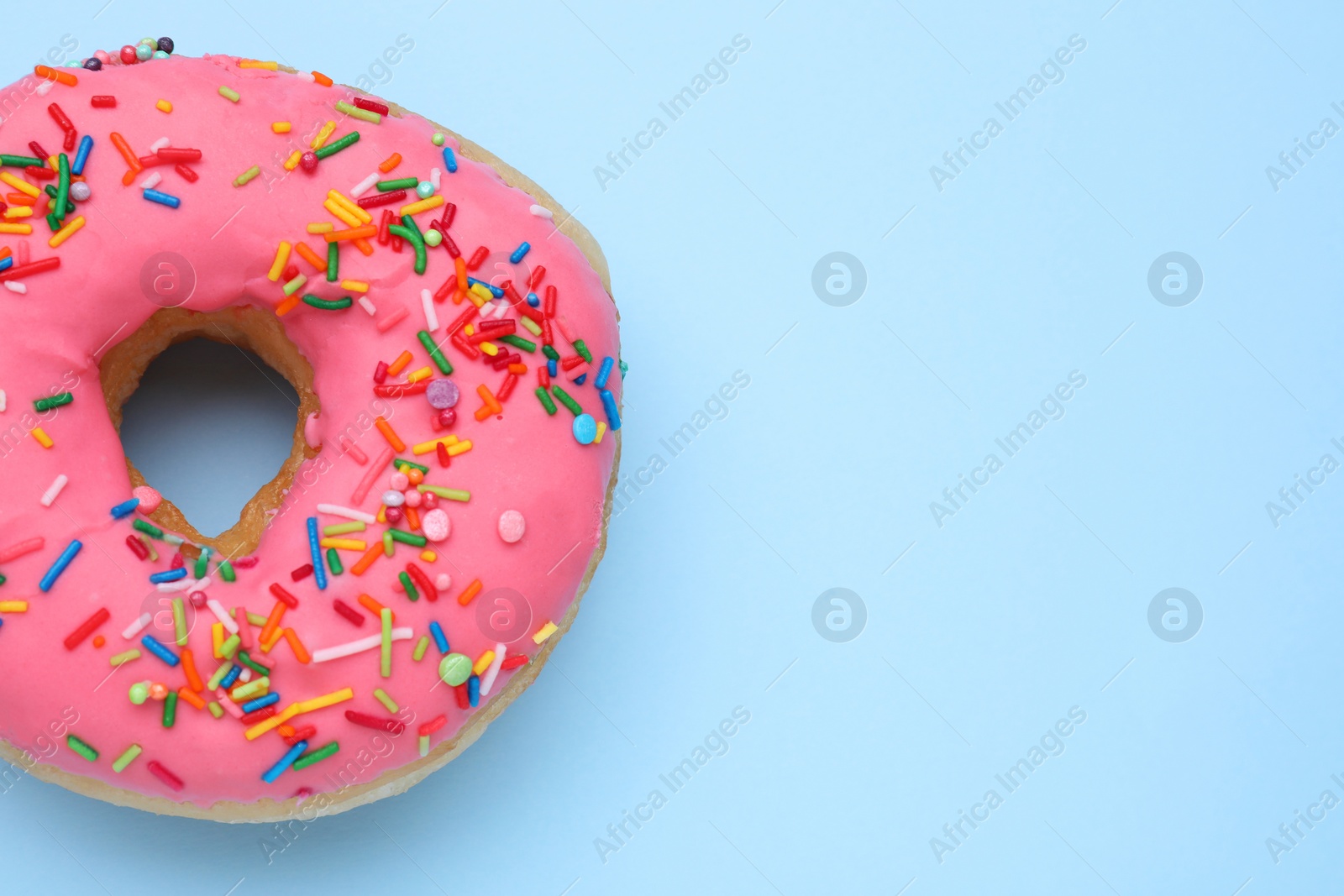 Photo of Glazed donut decorated with sprinkles on light blue background, top view. Space for text. Tasty confectionery