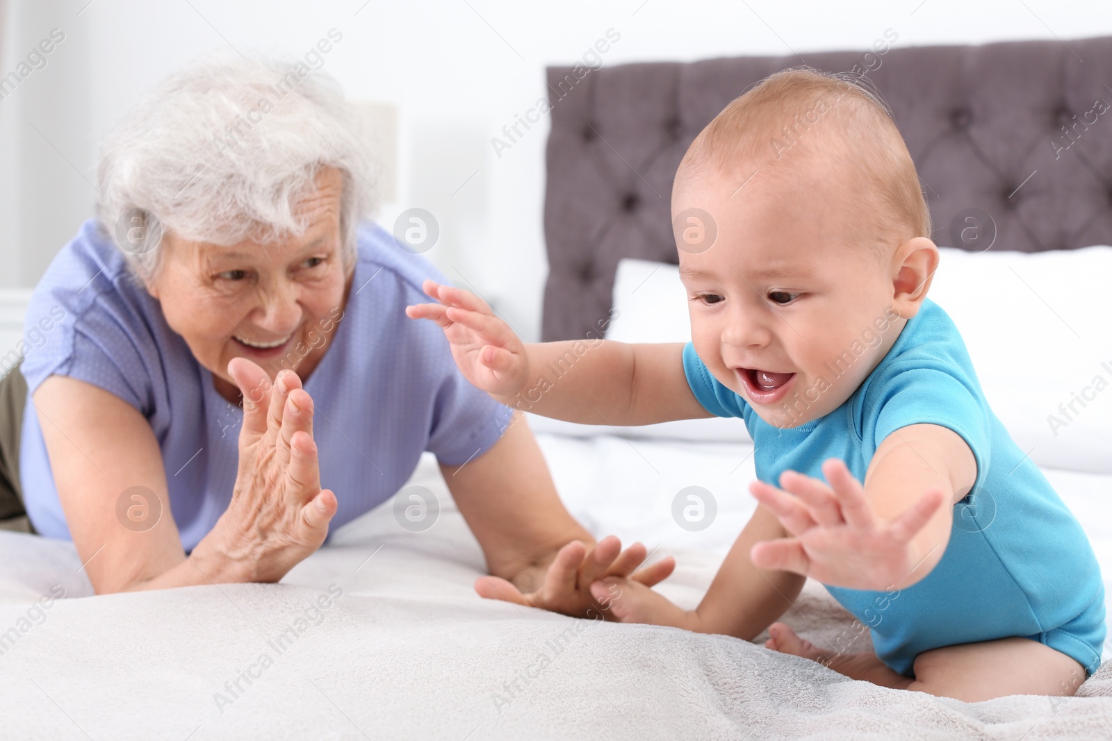 Photo of Cute little baby with happy grandmother in bedroom