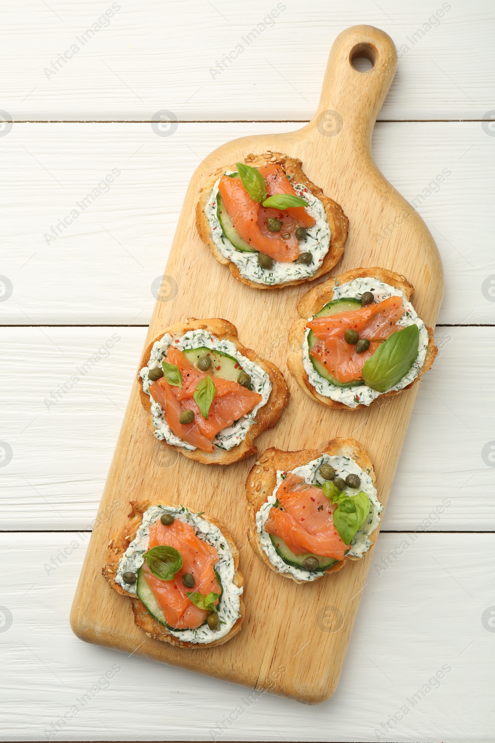 Photo of Tasty canapes with salmon, capers, cucumber and sauce on white wooden table, top view