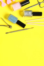 Nail polishes and set of pedicure tools on yellow background, flat lay. Space for text