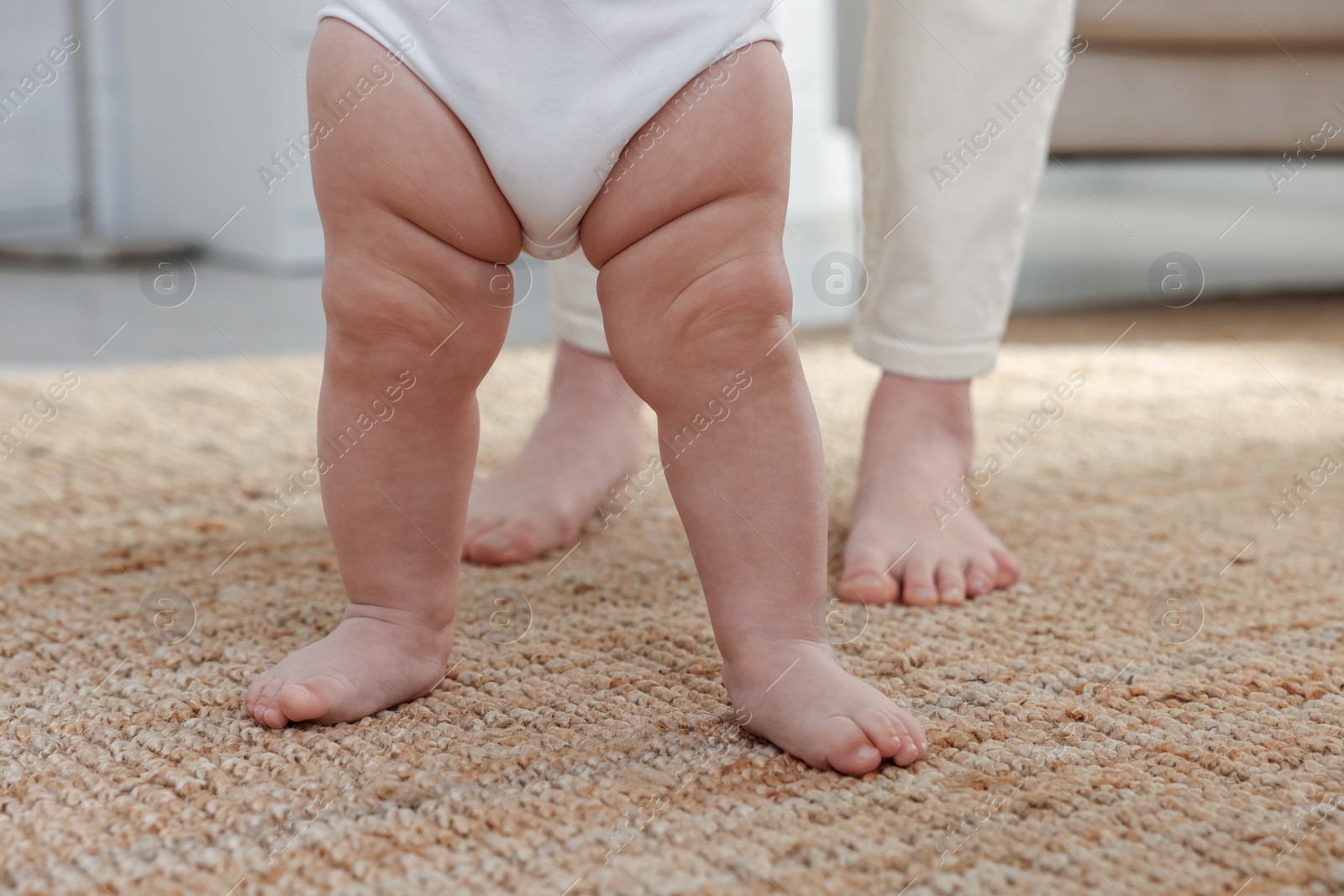 Photo of Cute little baby doing first steps with mother's help at home, closeup