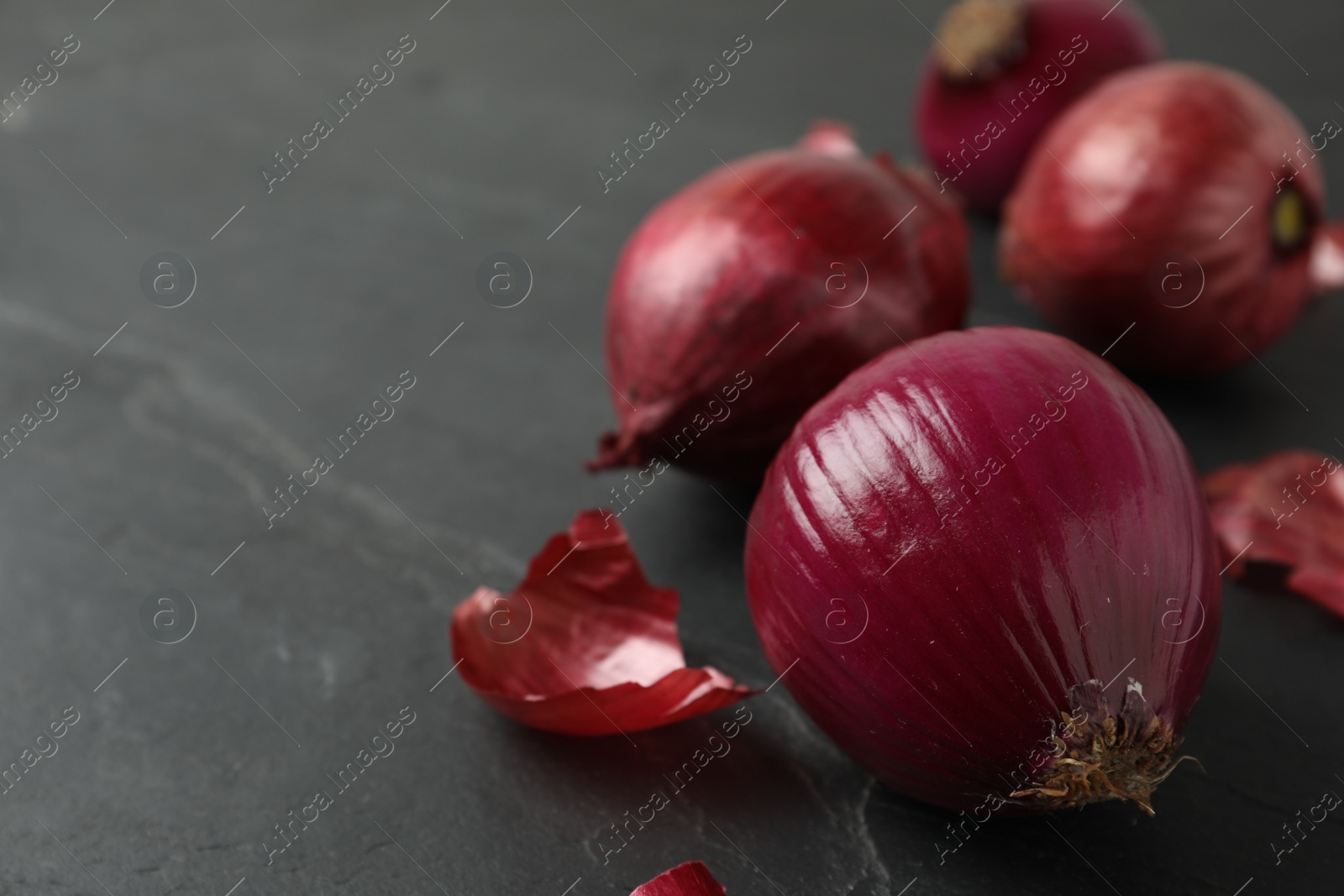 Photo of Ripe red onion bulbs on black slate table, closeup