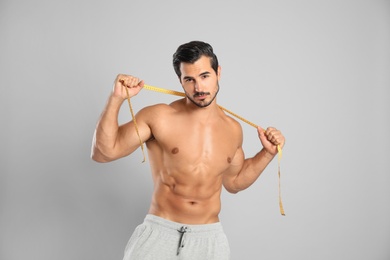 Photo of Young man with slim body using measuring tape on grey background