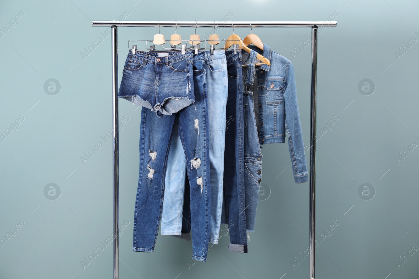 Photo of Rack with stylish jeans and denim clothes on color background